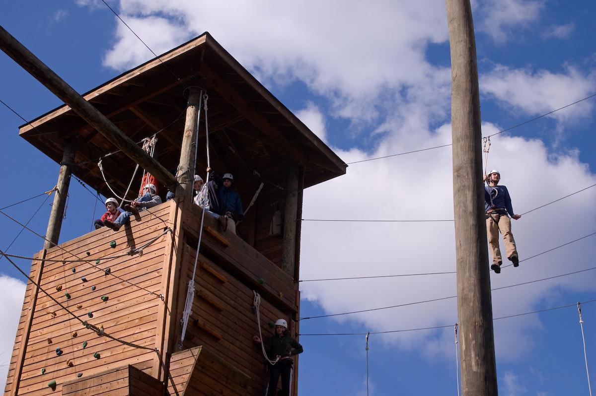 在bet8九州登录入口，学生们坐在岩壁上的高绳索课程塔上